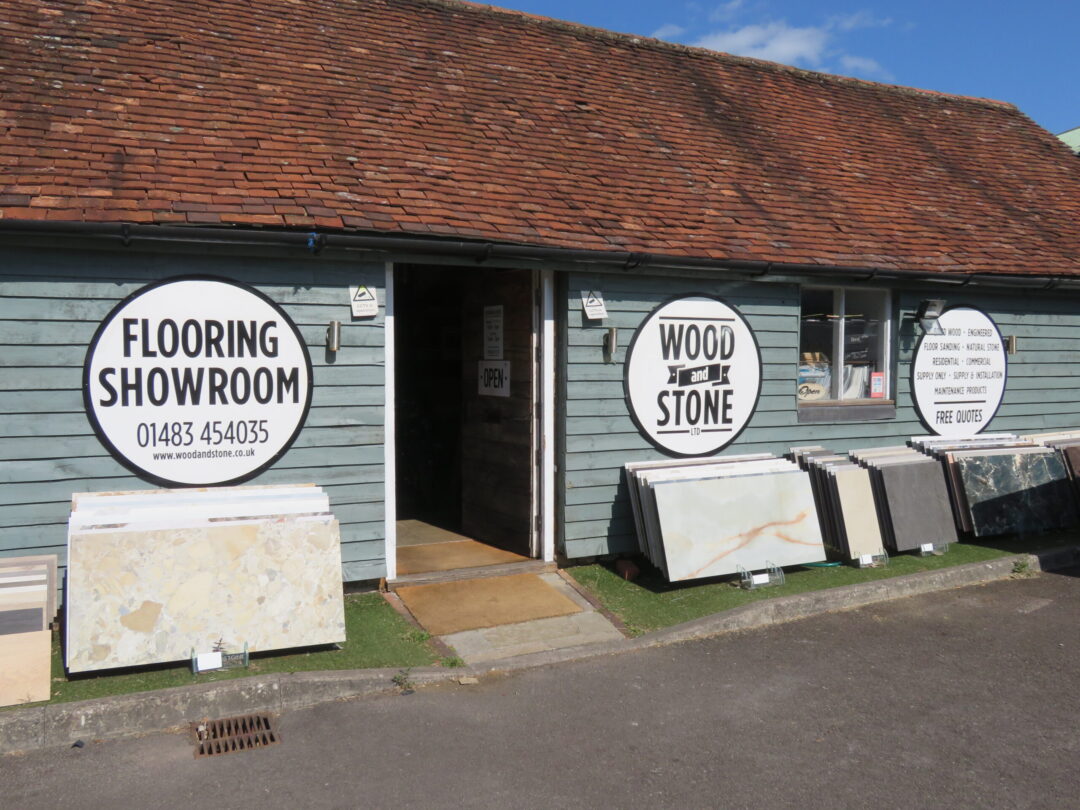 outside wood and stone showroom showing barn painted in light blue, front door open and sample off marble outside